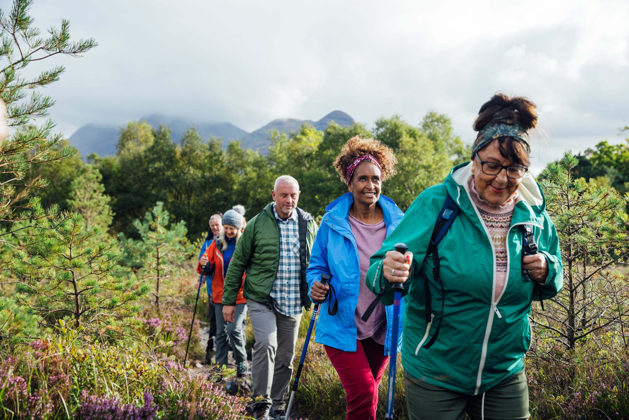 Wide front view of a medium group of mature and senior friends hiking up the mountain landscape surrounding Loch Torridon in the Northwest Highlands, Scotland. They are using hiking poles.