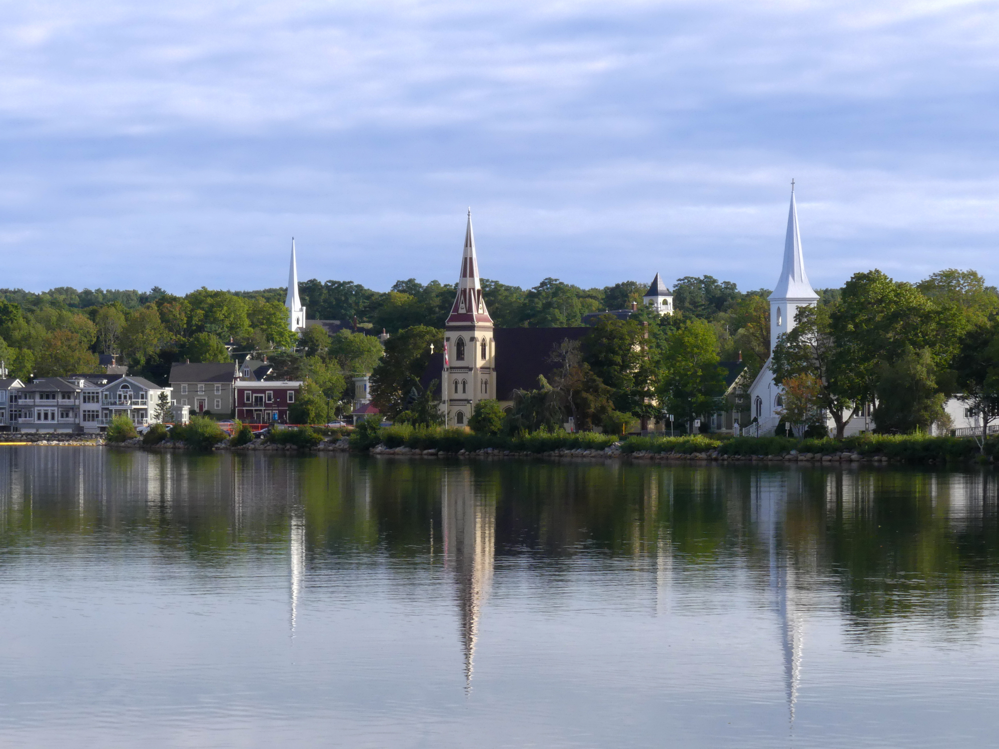 The serene coastal town of Mahone Bay presents a picturesque scene captured in this photo. Dominating the skyline are the iconic three churches that stand proudly against the backdrop of a clear blue sky.