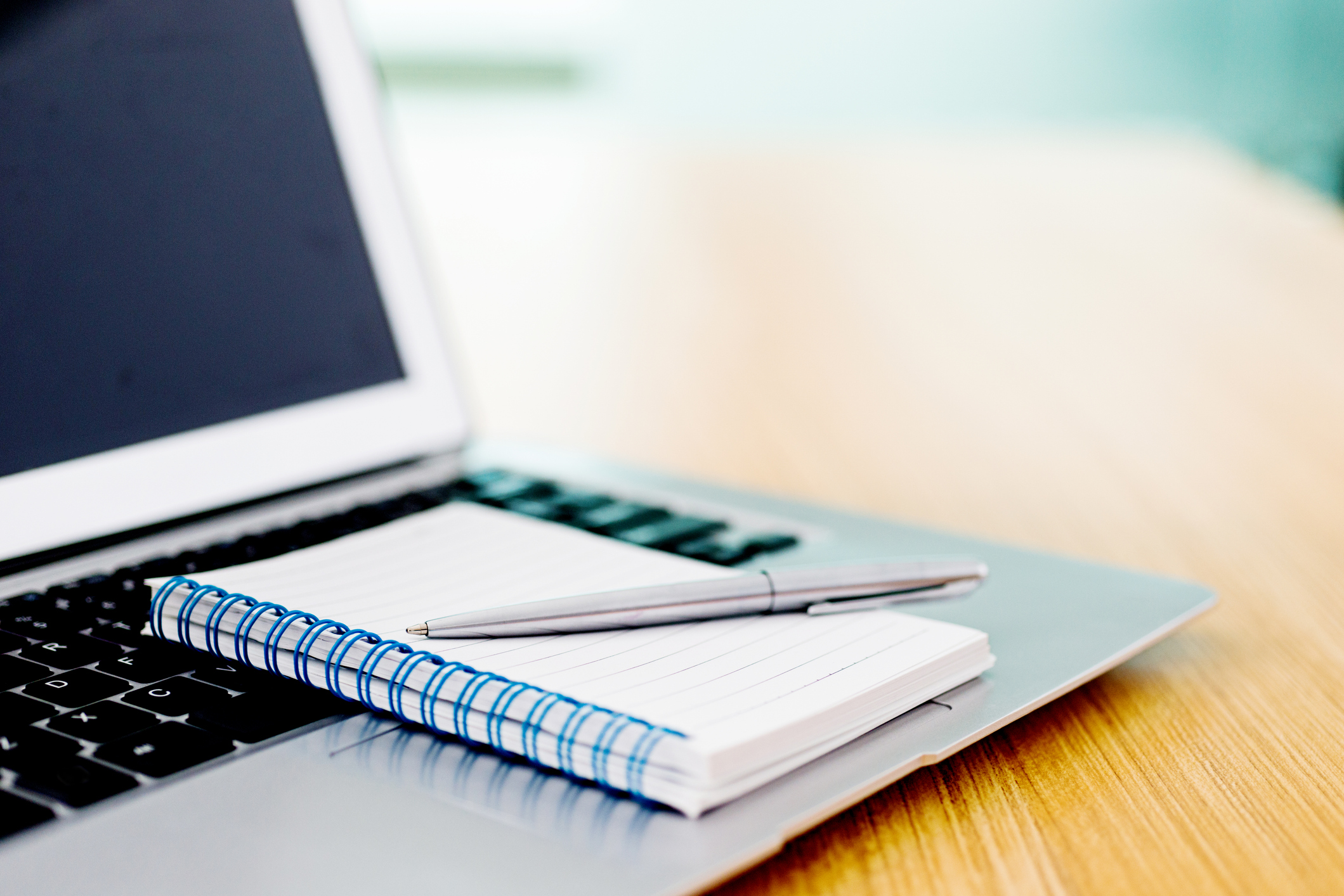 Laptop with pen and spiral notebook on desk.